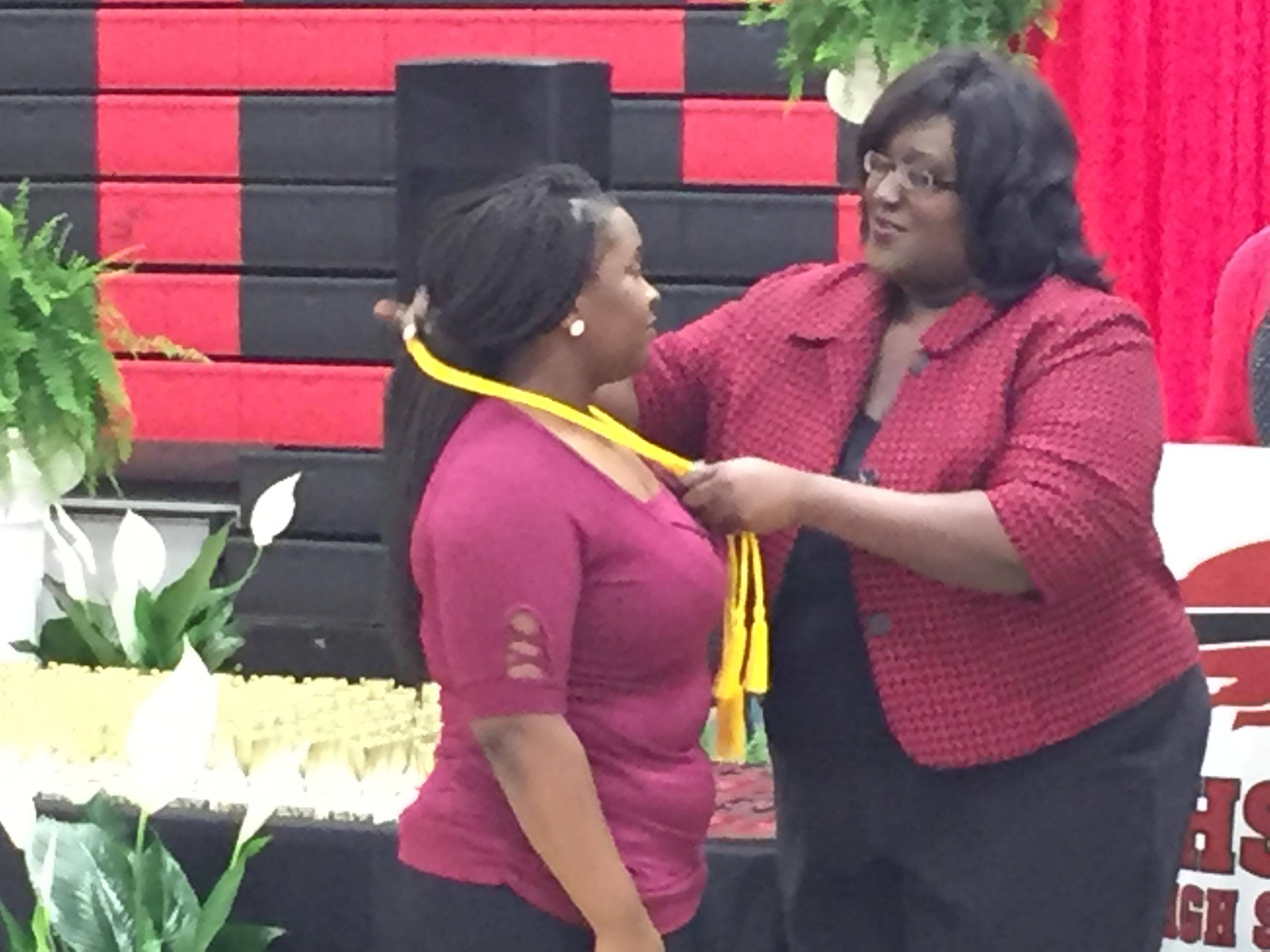 Photo of Miss Morgan and Doctor Russell placing honor cord around neck of a student