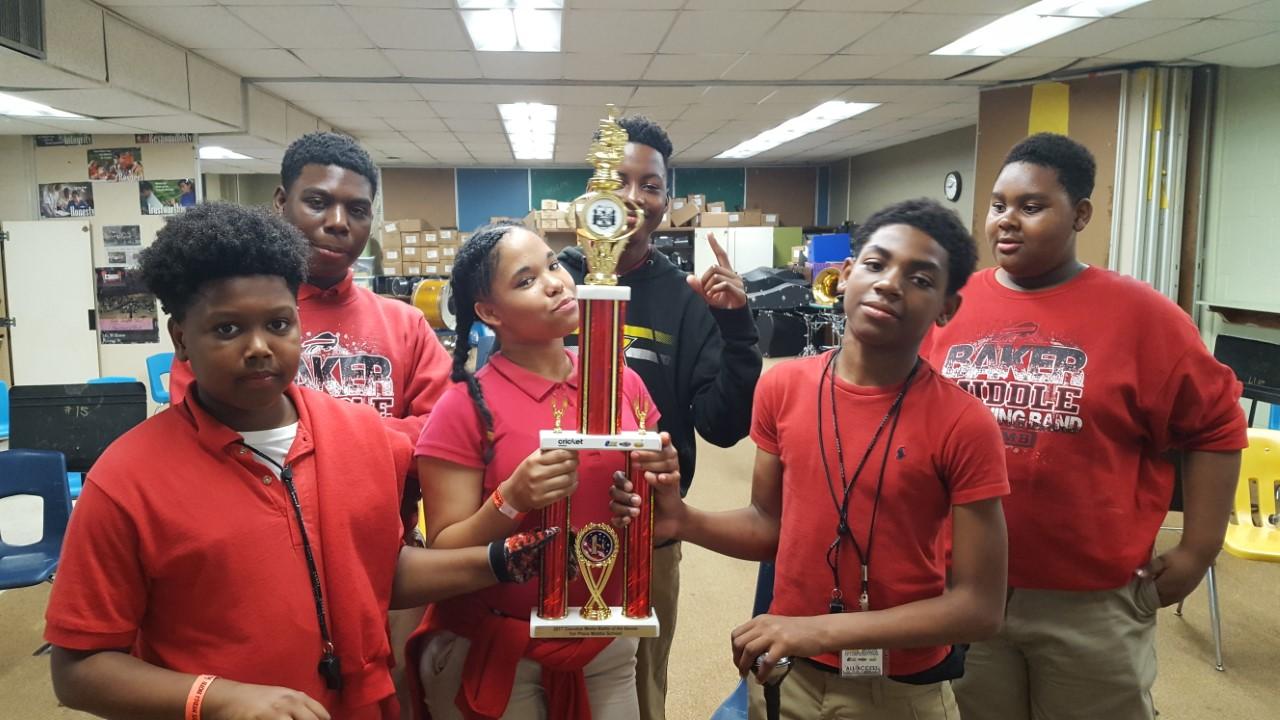 Six Baker Middle Band Students hold winning trophy from battle of the bands