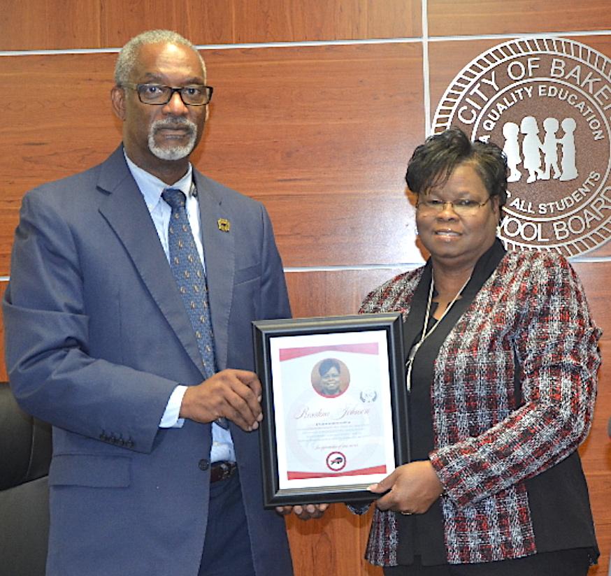 Photo of School System President Dr. Herman Brister presenting an award to outgoing Board Chairman Rosatina Johnson thanking her for service at the board's meeting on Tuesday.