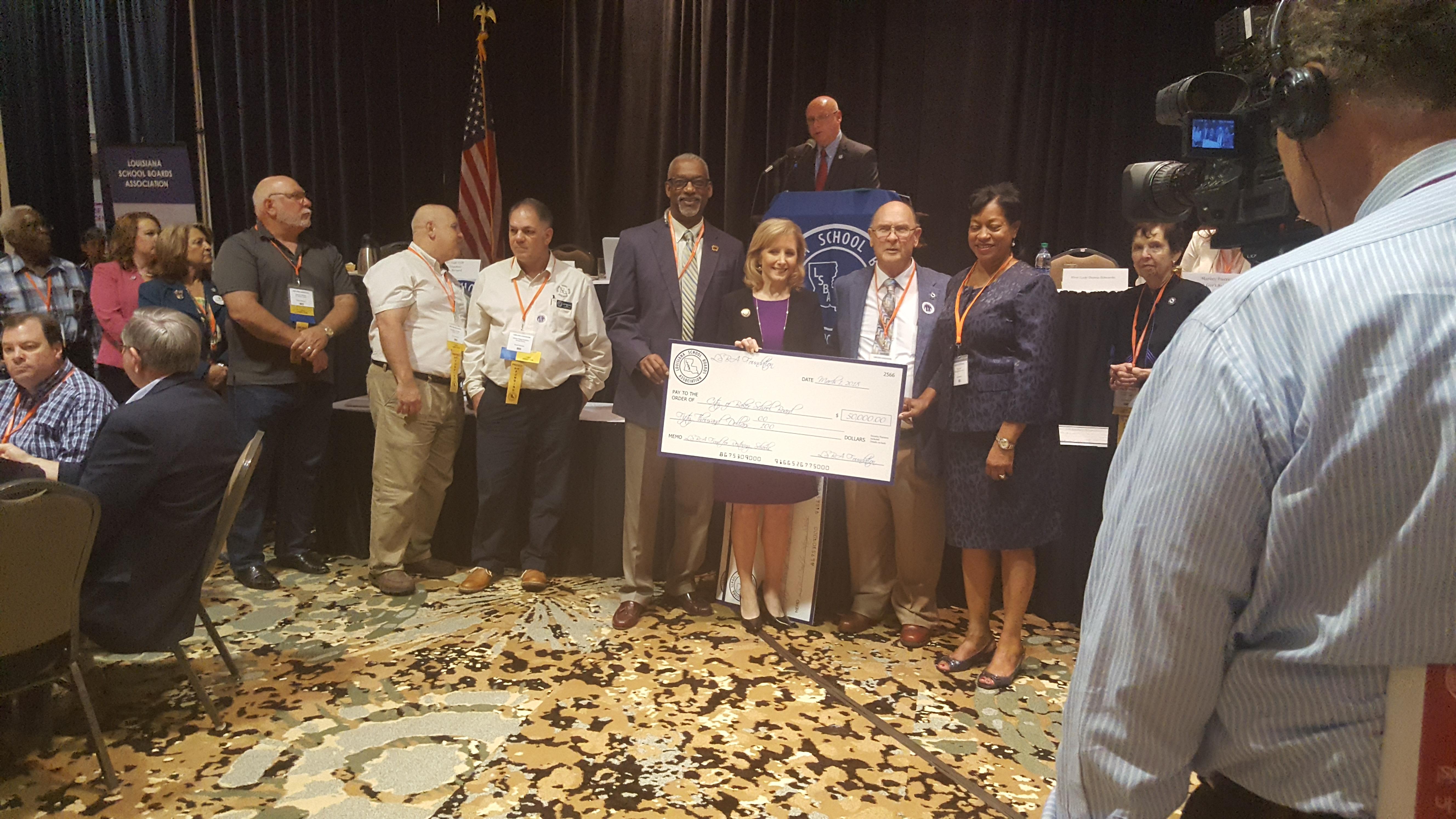 a photo of a officials with Dr. Brister at the LA School Board Association annual meeting. Dr. Brister is receiving a donation of $50,000 for the Baker District