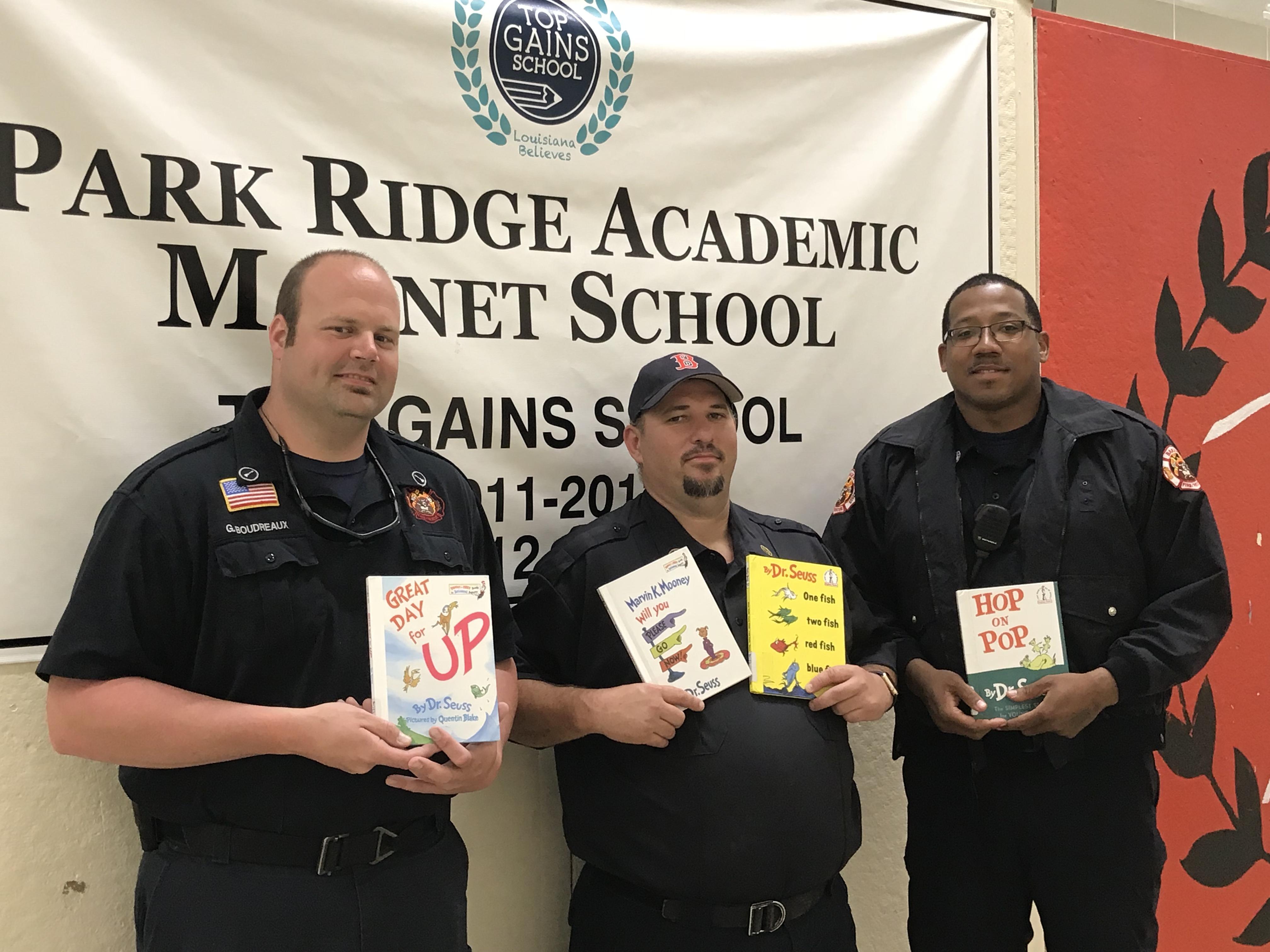 a photo of 3 members of the Baker Fire Department holding a book in hallway at Park Ridge for national reading day ..