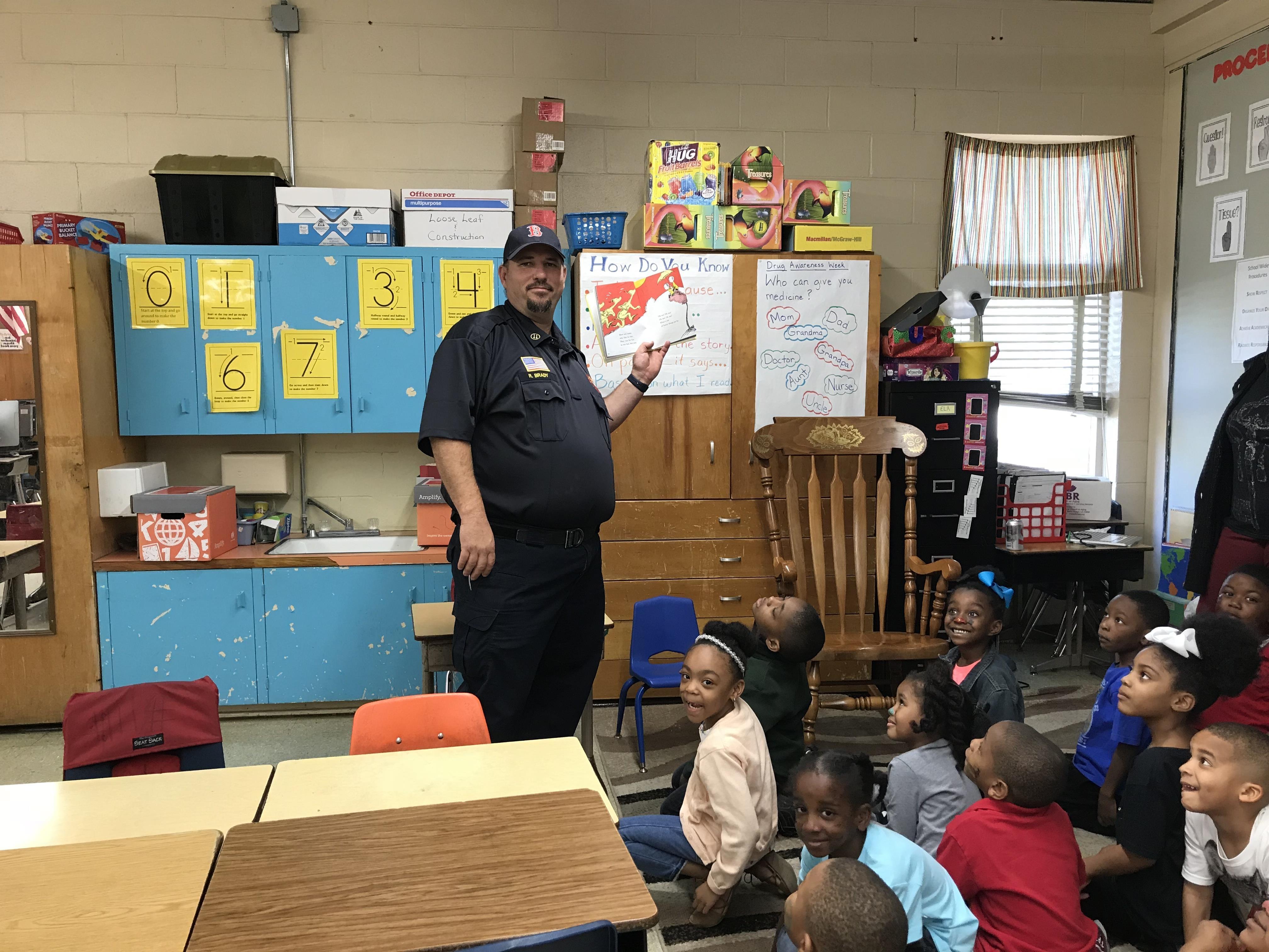 a photo of one member of the Baker Fire Department reading to a classroom of students at Park Ridge Academic Magnet School