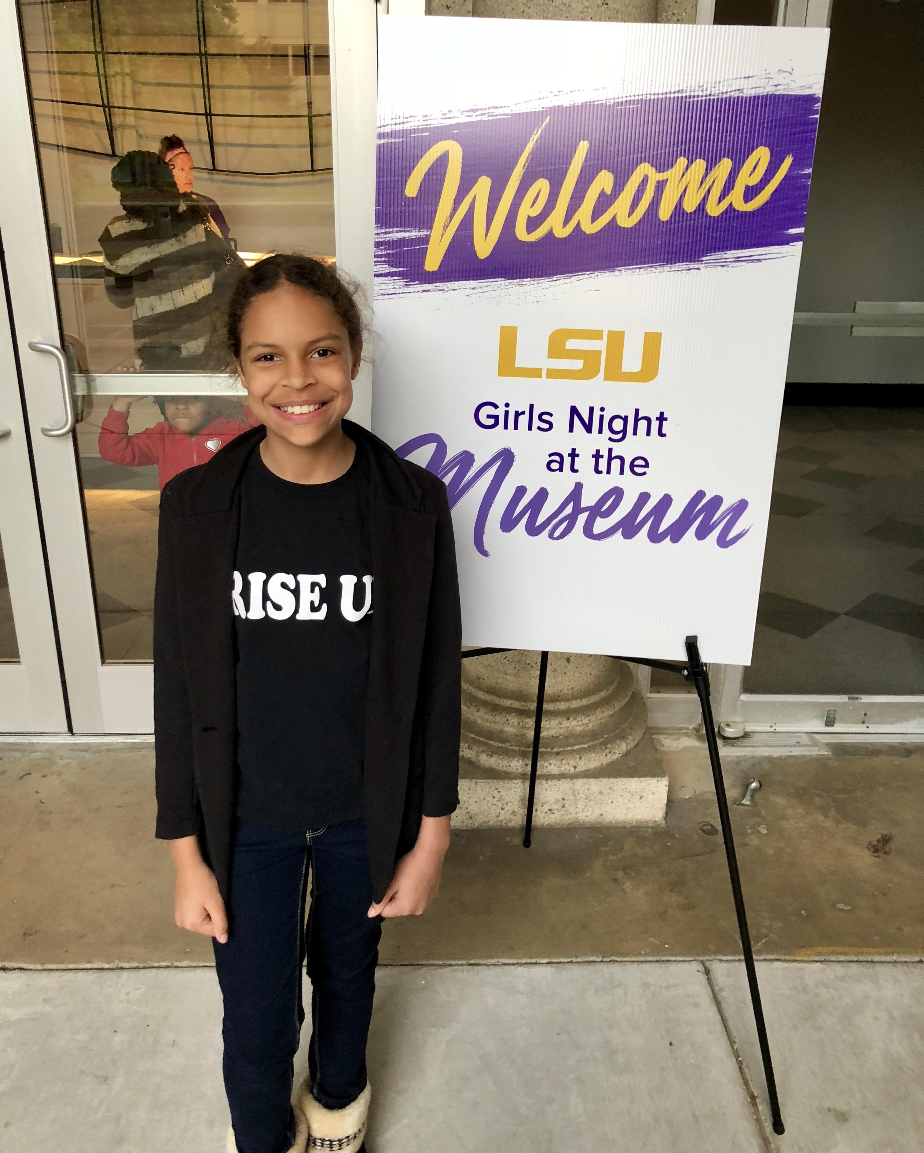 a photo of one of City of Baker Girls in front of a poster sign at the LSU Girls Night at the Museum
