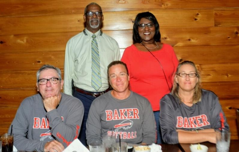 A photo of the Baker High School Softball Coaches seated at a restaurant table with the Superintendent and their Principal standing behind them