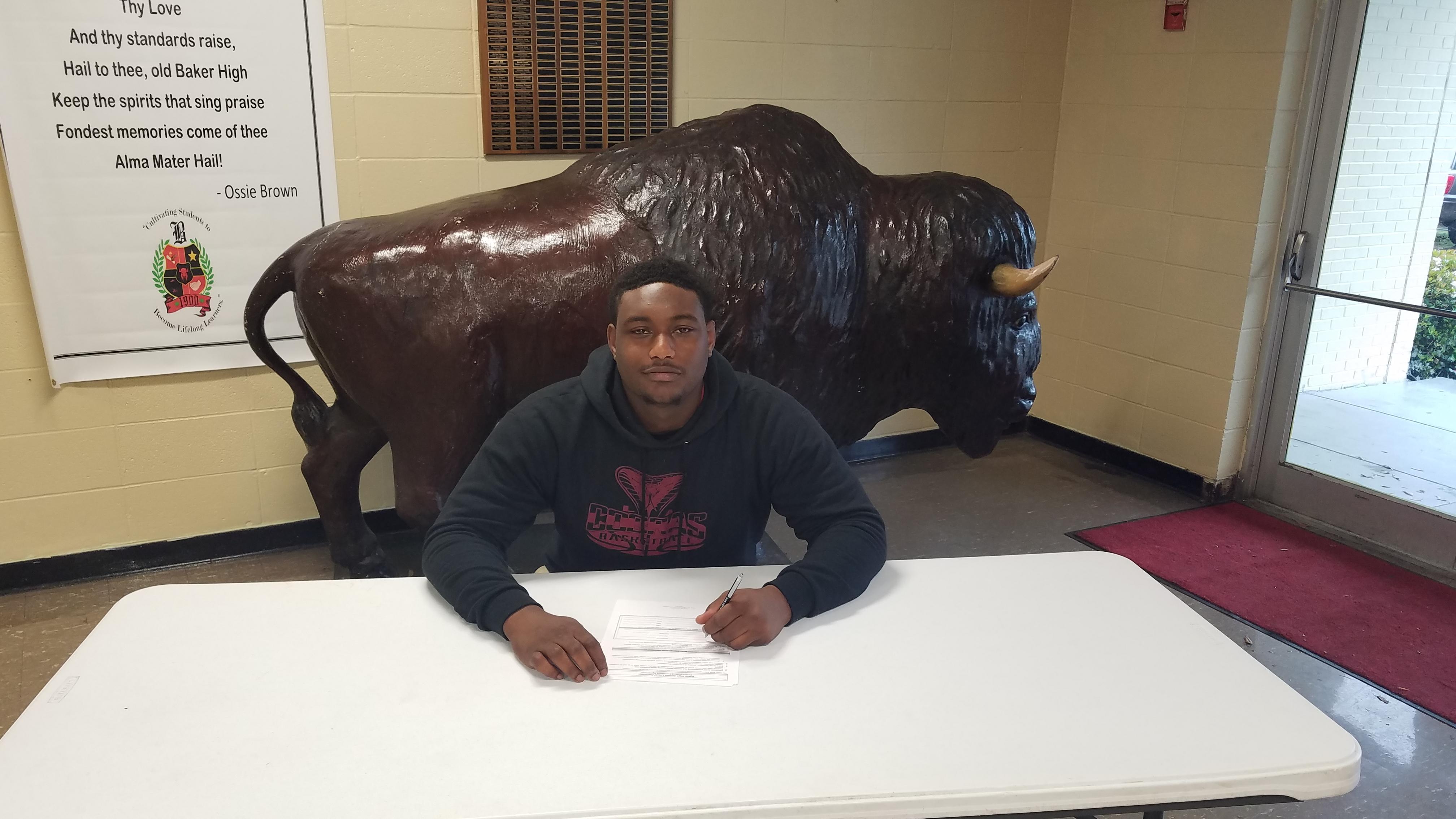 a photo of Baker High School Athlete, Jalen Gross, preparing to sign a commitment to play football for East Central Mississippi Community College